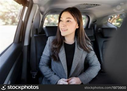 happy young business woman thinking and looking view out of window while sitting in the back seat of car