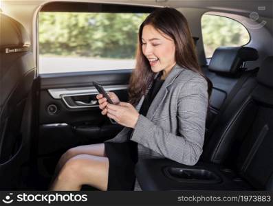 happy young business woman using a smartphone while sitting in the back seat of car