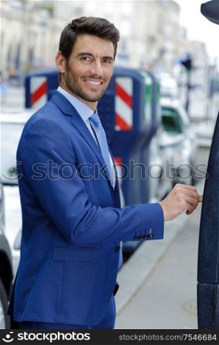 happy young businessman inserting coin into parking machine