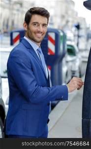 happy young businessman inserting coin into parking machine