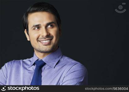Happy young businessman looking at copy space over black background