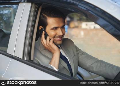 Happy young businessman on call while driving car