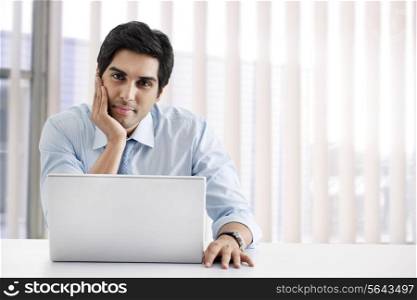 Happy young businessman sitting at his desk with laptop