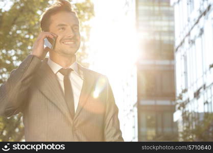 Happy young businessman using cell phone outdoors