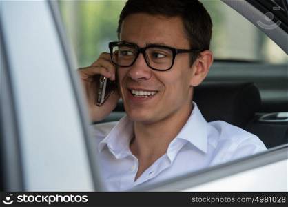 Happy young businessman using mobile phone in back seat of car