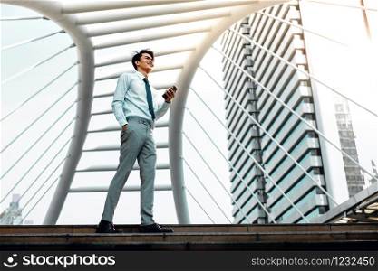 Happy Young Businessman Using Mobile Phone in the City. Lifestyle of Modern People. Low Angle View. Full Length. Modern Urban City as background