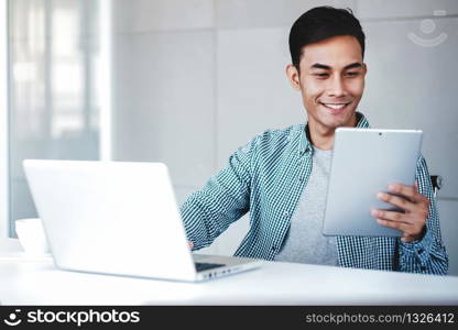 Happy Young Businessman Working on Computer Laptop and Digital Tablet in Office