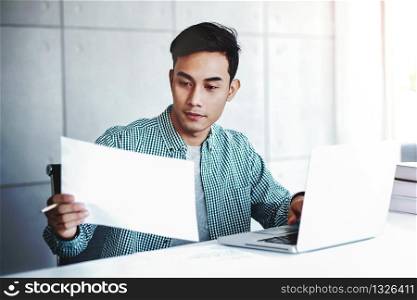 Happy Young Businessman Working on Computer Laptop and Document Paper in Office