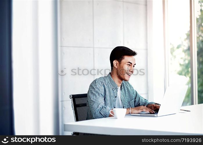 Happy Young Businessman Working on Computer Laptop in Office. Sitting on Desk, Man in Casual Wear