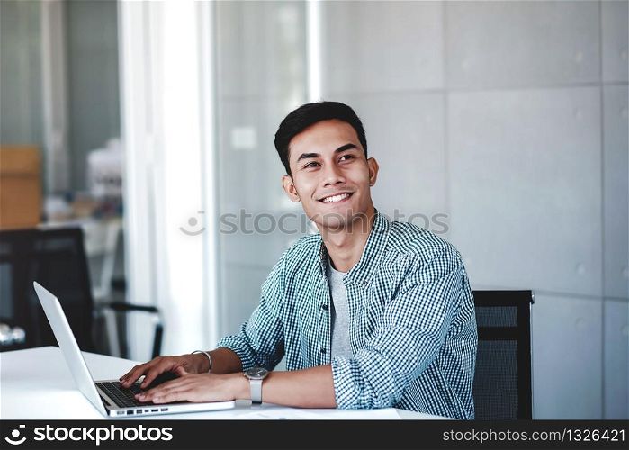 Happy Young Businessman Working on Computer Laptop in Office. Smiling and looking away