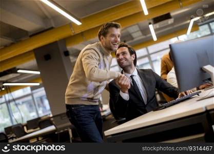 Happy young businessmen handshaking by the table in the modern office