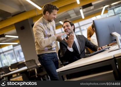 Happy young businessmen handshaking by the table in the modern office