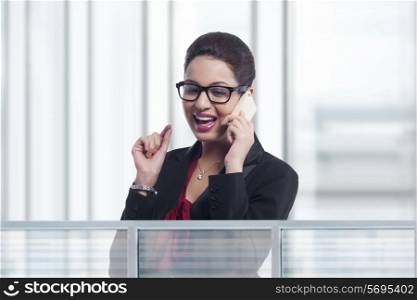 Happy young businesswoman answering mobile phone in office