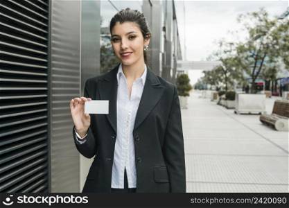 happy young businesswoman standing outside office building showing her business card
