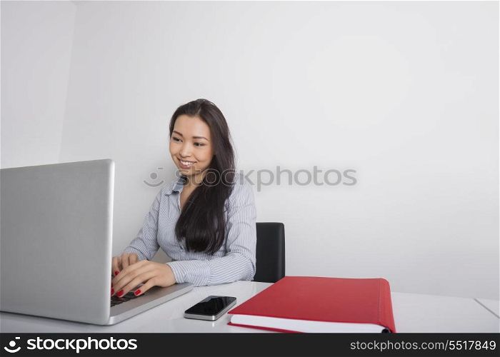 Happy young businesswoman using laptop at office desk