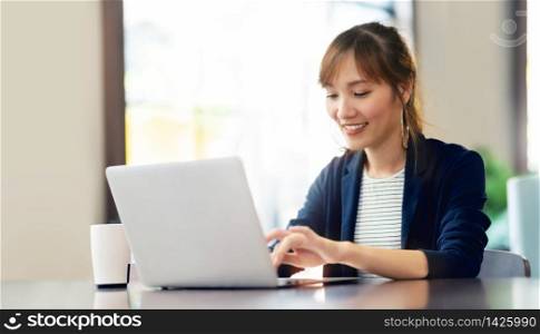Happy young businesswoman using laptop computer doing online shopping at cafe. Smiling beautiful Asian woman sitting and working at her workplace. Lifestyle, Technology, Internet, Wireless communication.