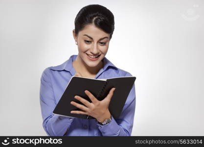 Happy young businesswoman writing on note pad against gray background