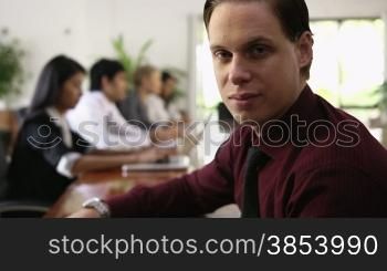 Happy young caucasian businessman smiling at camera during business meeting with colleagues. Rack focus