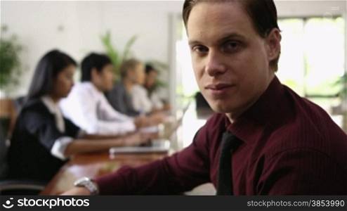 Happy young caucasian businessman smiling at camera during business meeting with colleagues. Rack focus