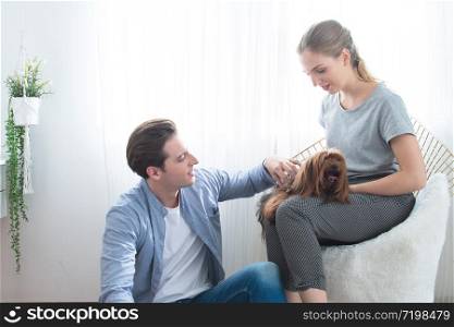 Happy young caucasian couple petting and embracing their brown puddle on the couch at home in the living room. happy young caucasian couple play with dog in home