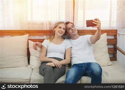 Happy young caucasian couple sit on the couch taking selfie at home in the living room,romance moment of man and woman in leisure time.