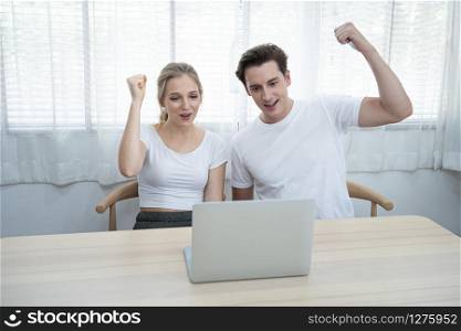 Happy young caucasian couple with laptop hand rise up with happy and fun moment spending time together at home.