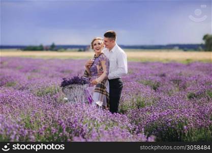 Happy young couple are walking with retro bicycle in lavender field. woman in purple dress and with hairstyle is hugging her man outdoors.. Happy young couple are walking with retro bicycle in lavender field. man is hugging her woman in purple dress and with hairstyle outdoors