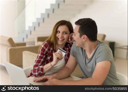 happy young couple buying online using laptop a computer and a credit card in their luxury home villa