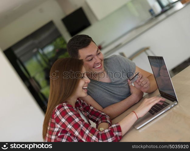 happy young couple buying online using laptop a computer and a credit card in their luxury home villa