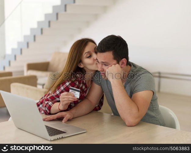 happy young couple buying online using laptop a computer and a credit card in their luxury home villa