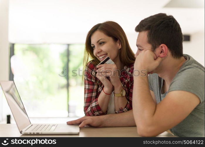 happy young couple buying online using laptop a computer and a credit card in their luxury home villa