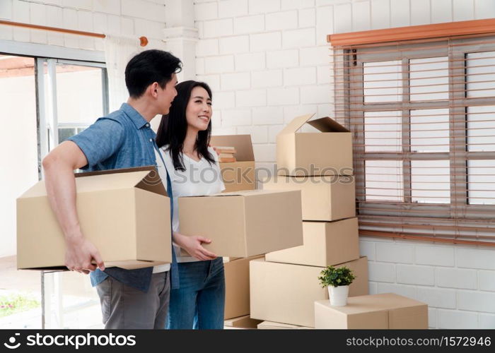 Happy young couple Carrying cardboard boxes and walking from the front door into the house in a new house at moving day. Concept of relocation, rental, and homeowner moving at home.