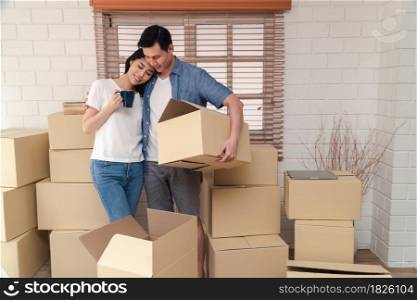 Happy young couple Carrying cardboard boxes and walking from the front door into the house in a new house at moving day. Concept of relocation, rental, and homeowner moving at home.