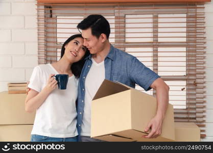 Happy young couple Carrying cardboard boxes and walking from the front door into the house in a new house at moving day. Concept of relocation, rental, and homeowner moving at home.