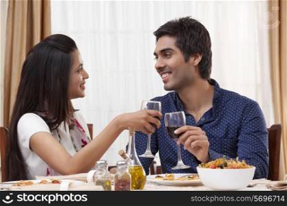 Happy young couple clinking wine glass while looking at each other at restaurant
