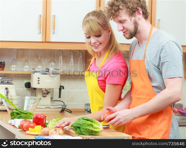 Happy young couple cooking. Woman and man having fun in modern kitchen indoor at home while preparing fresh vegetables food salad