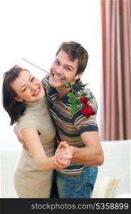 Happy young couple dancing with red rose at home