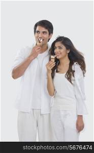 Happy young couple eating ice creams cones while looking away over white background