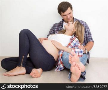 Happy young couple expecting baby sitting on floor at living room