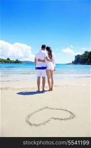 happy young couple have fun and relax on the summer with heart drawing on beach sand