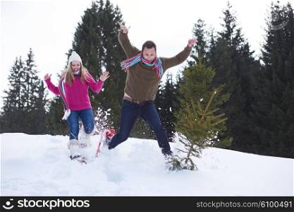 happy young couple having fun and walking in snow shoes outdoor in nature at beautiful winter day. Health sport and relaxation