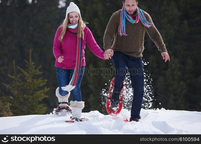 happy young couple having fun and walking in snow shoes outdoor in nature at beautiful winter day. Health sport and relaxation