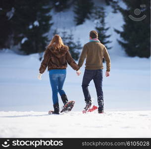 happy young couple having fun and walking in snow shoes. Romantic winter relaxation scene