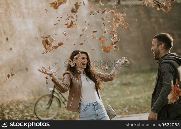 Happy young couple having fun with autumn leaves in the park