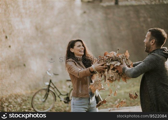 Happy young couple having fun with autumn leaves in the park
