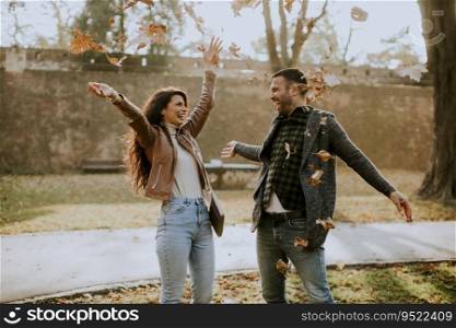 Happy young couple having fun with autumn leaves in the park