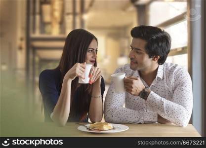 Happy young couple having hot drink at restaurant table