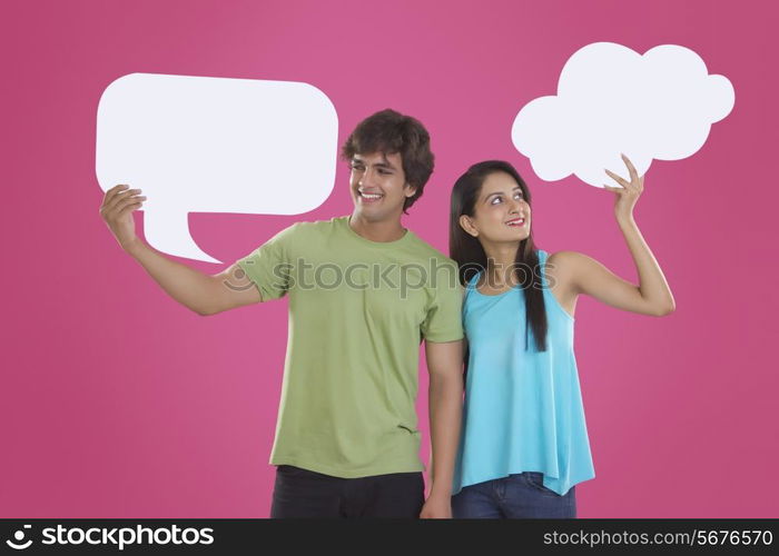 Happy young couple holding communication bubbles over pink background