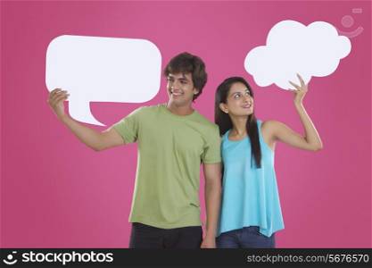Happy young couple holding communication bubbles over pink background