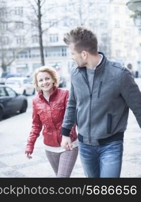 Happy young couple holding hands while walking on city street